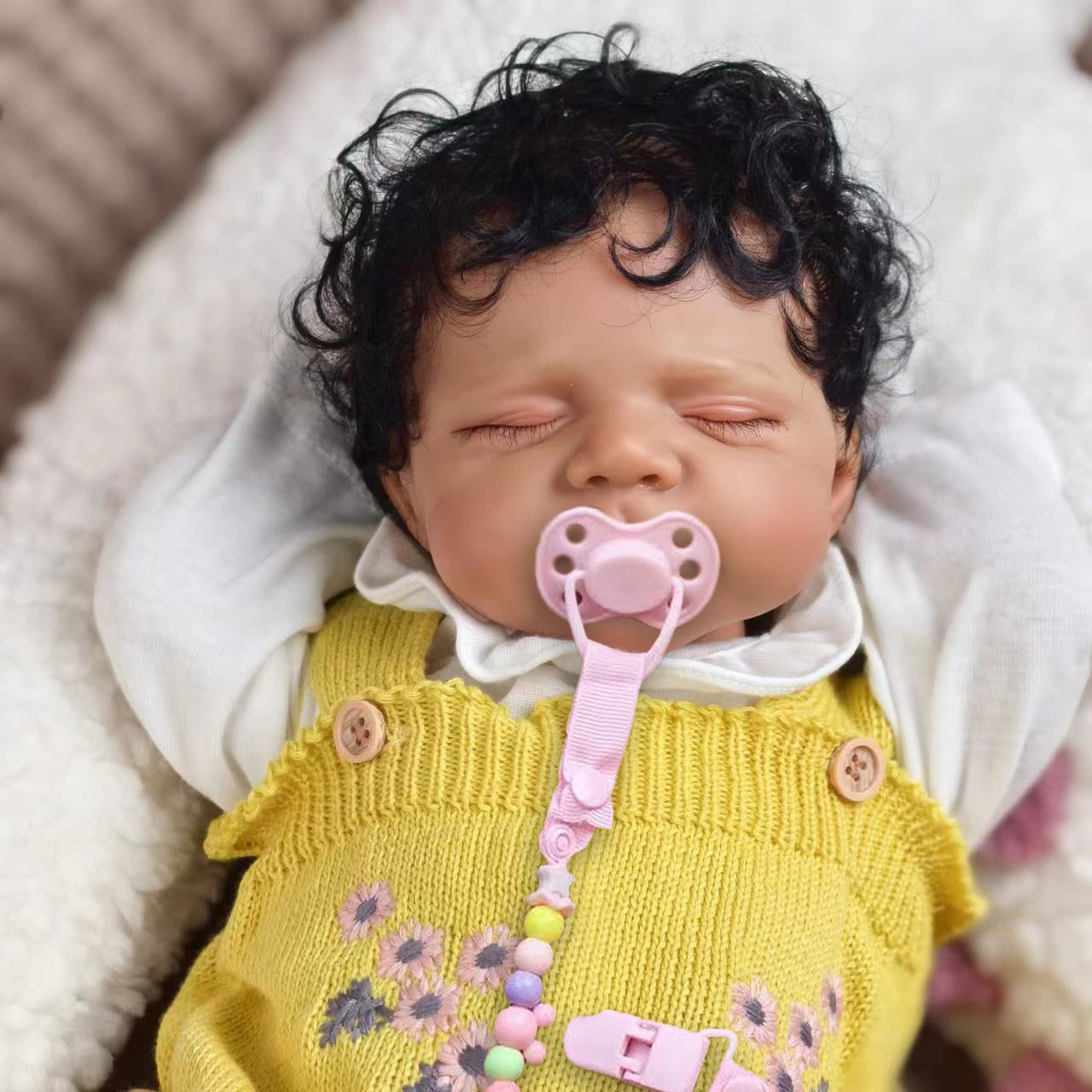 KEIUMI reborn baby doll sleeping peacefully in a yellow knitted romper.