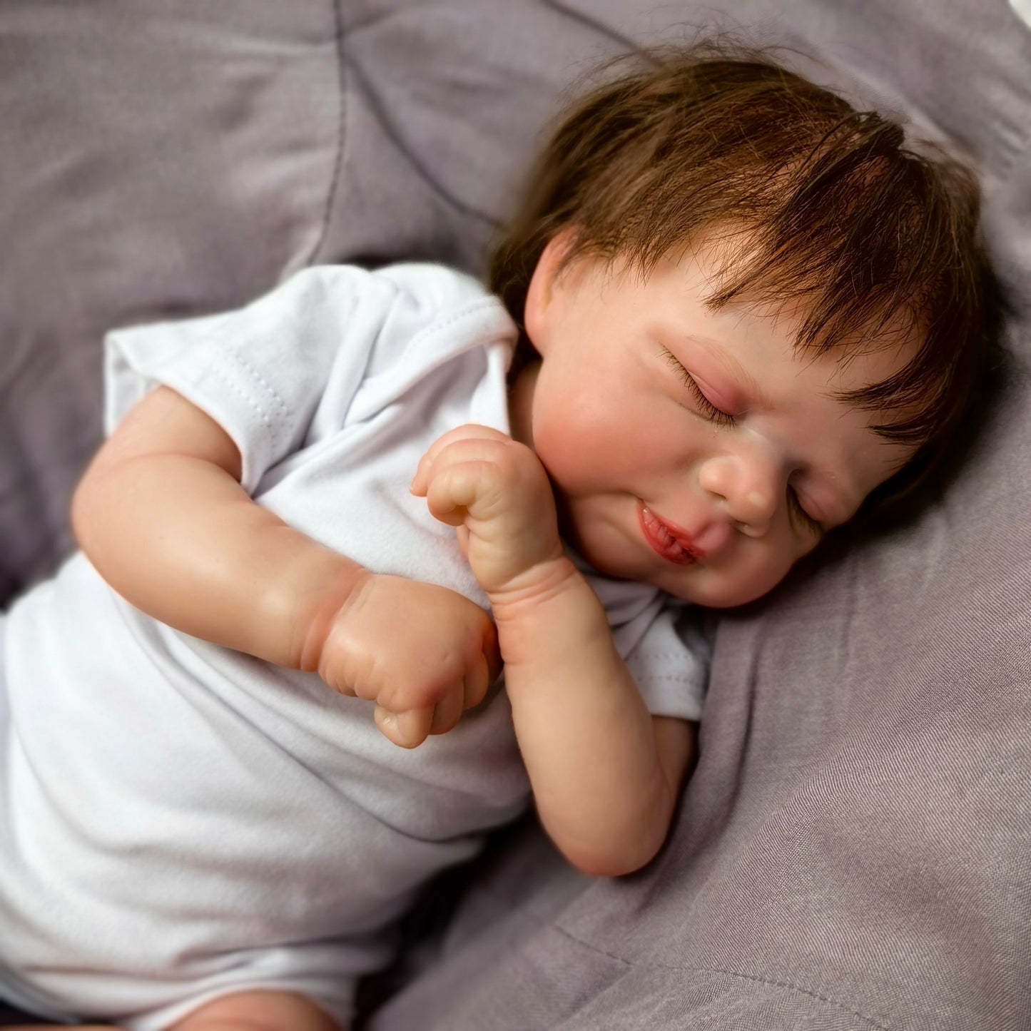 Realistic reborn baby doll's tiny hand resting on its chest.