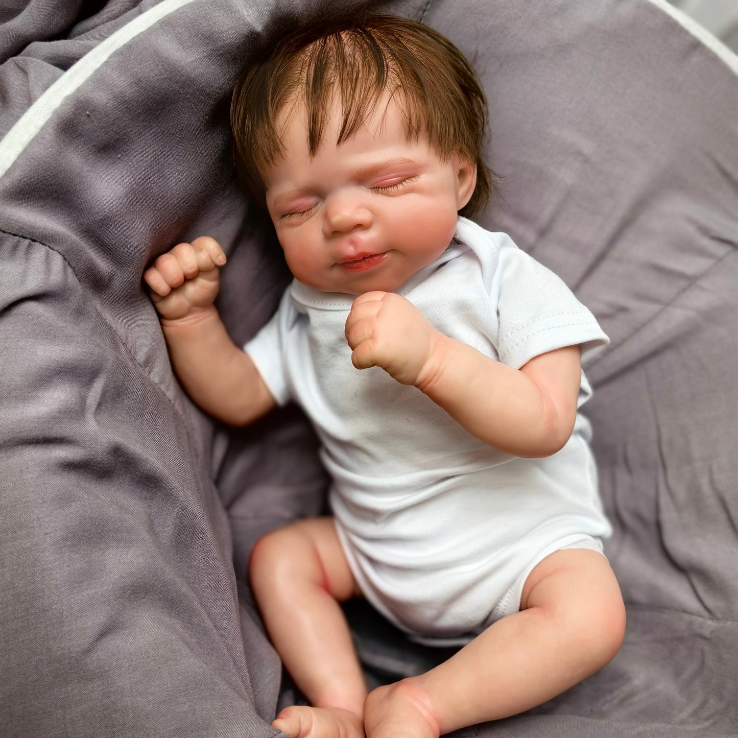Close-up of sleeping reborn baby doll's lifelike face and dark brown hair.