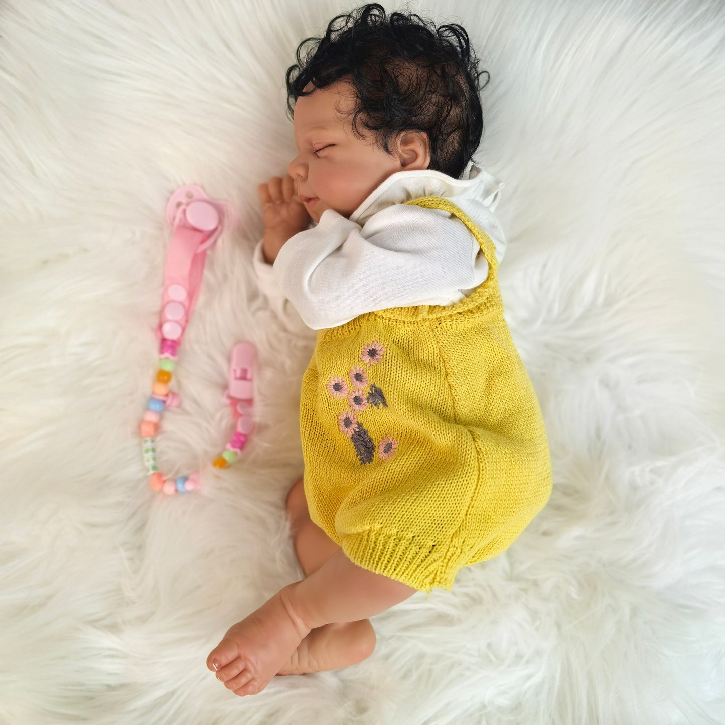 Reborn baby doll's hand holding a pink pacifier with colorful beads.