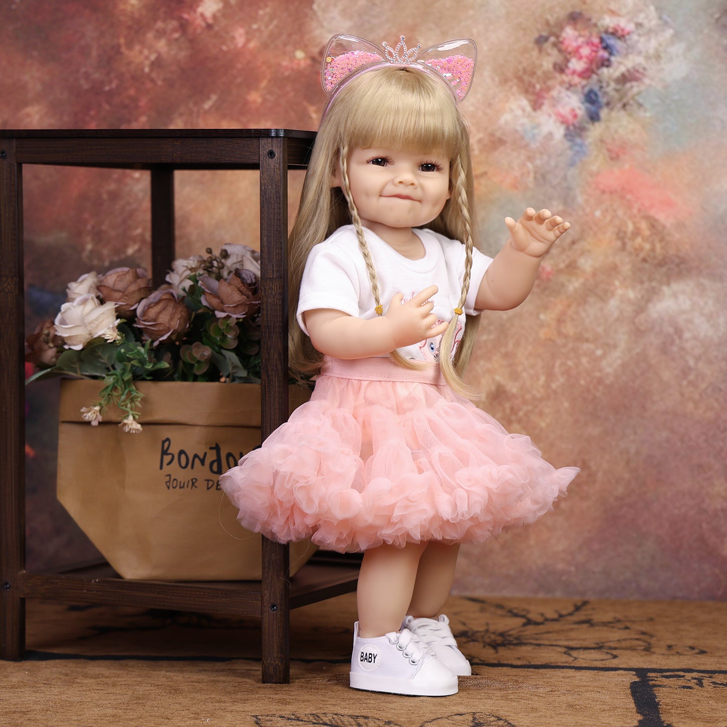 KEIUMI reborn doll's feet in white sneakers with 'BABY' text, pink ruffled skirt.