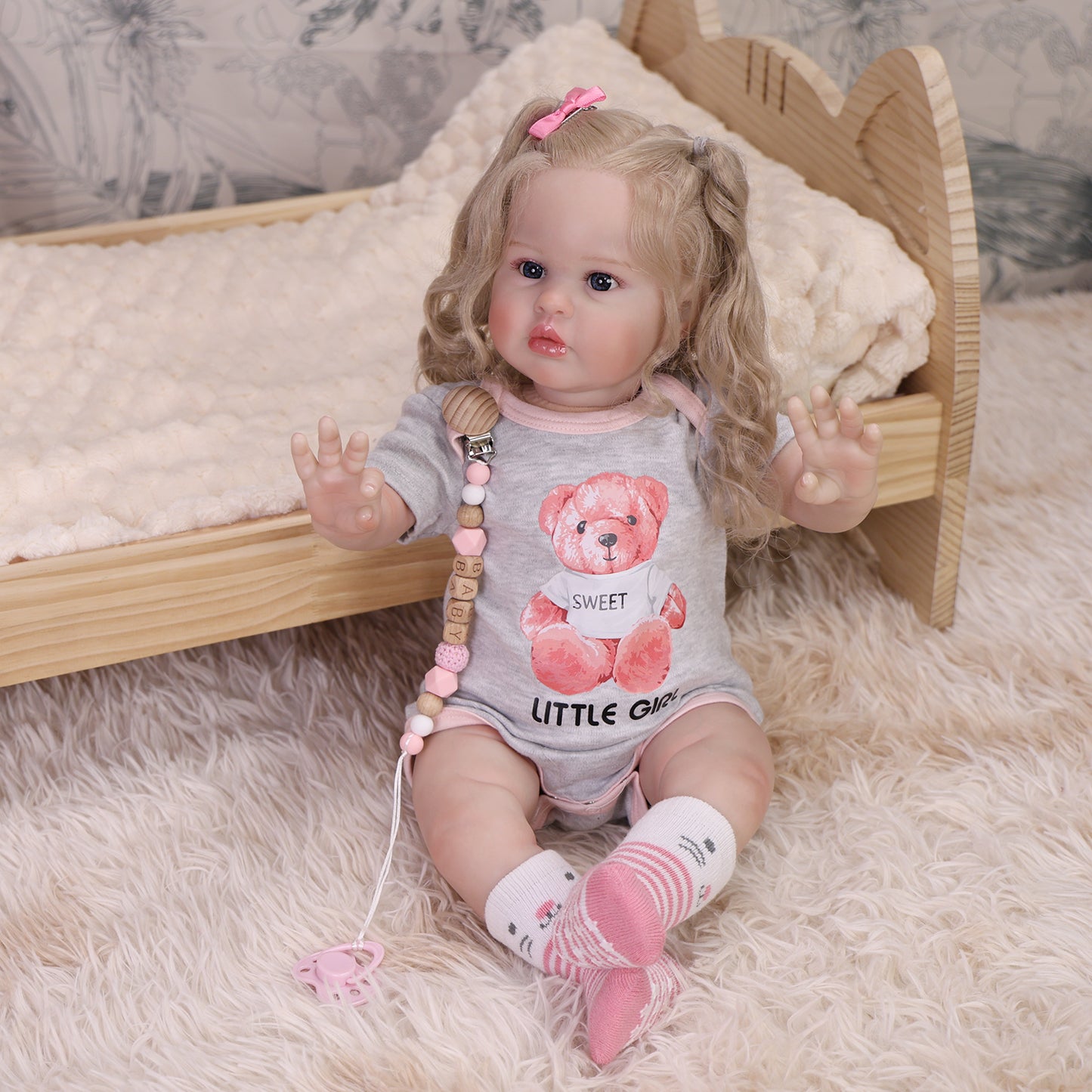 Penny reborn doll in grey onesie with pink trim, holding a pink pacifier.