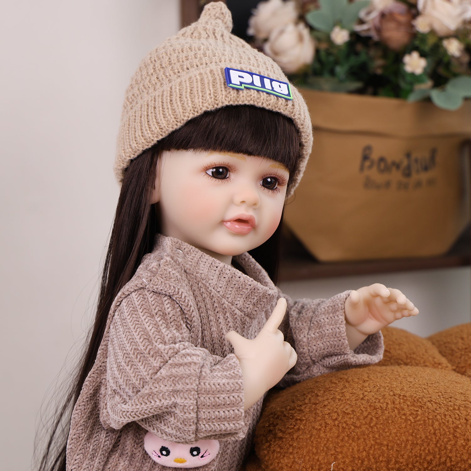 KEIUMI reborn doll sitting, showcasing her full knitted outfit and beige beanie.