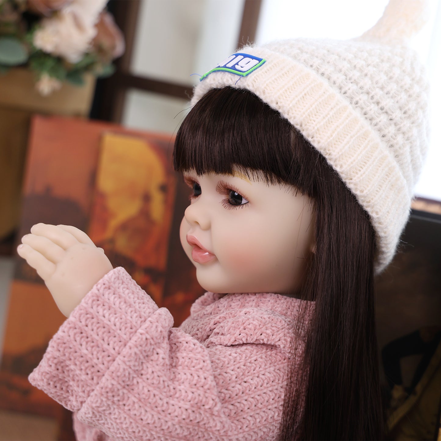 KEIUMI Elara doll sitting, showing her pink knitted romper and cream beanie.