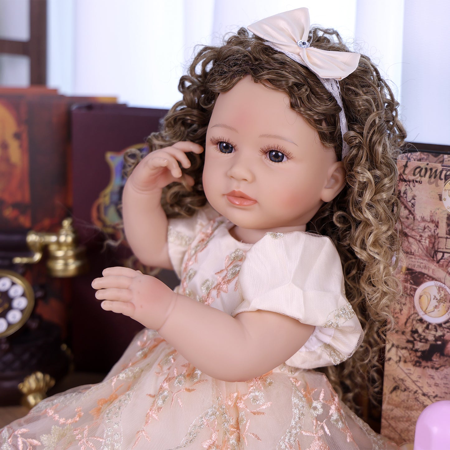 Emmeline reborn doll sitting, holding a pink baby bottle, displaying her detailed outfit.