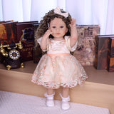 Back view of Emmeline reborn doll's embroidered gown and bouncy brown curly hair.