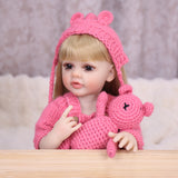 Maisie reborn doll sitting, showing full pink knitted outfit and white sneakers.