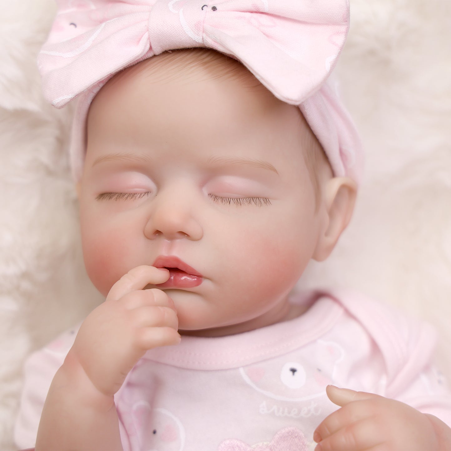 Realistic sleeping reborn doll in pink outfit, showing full body detail.