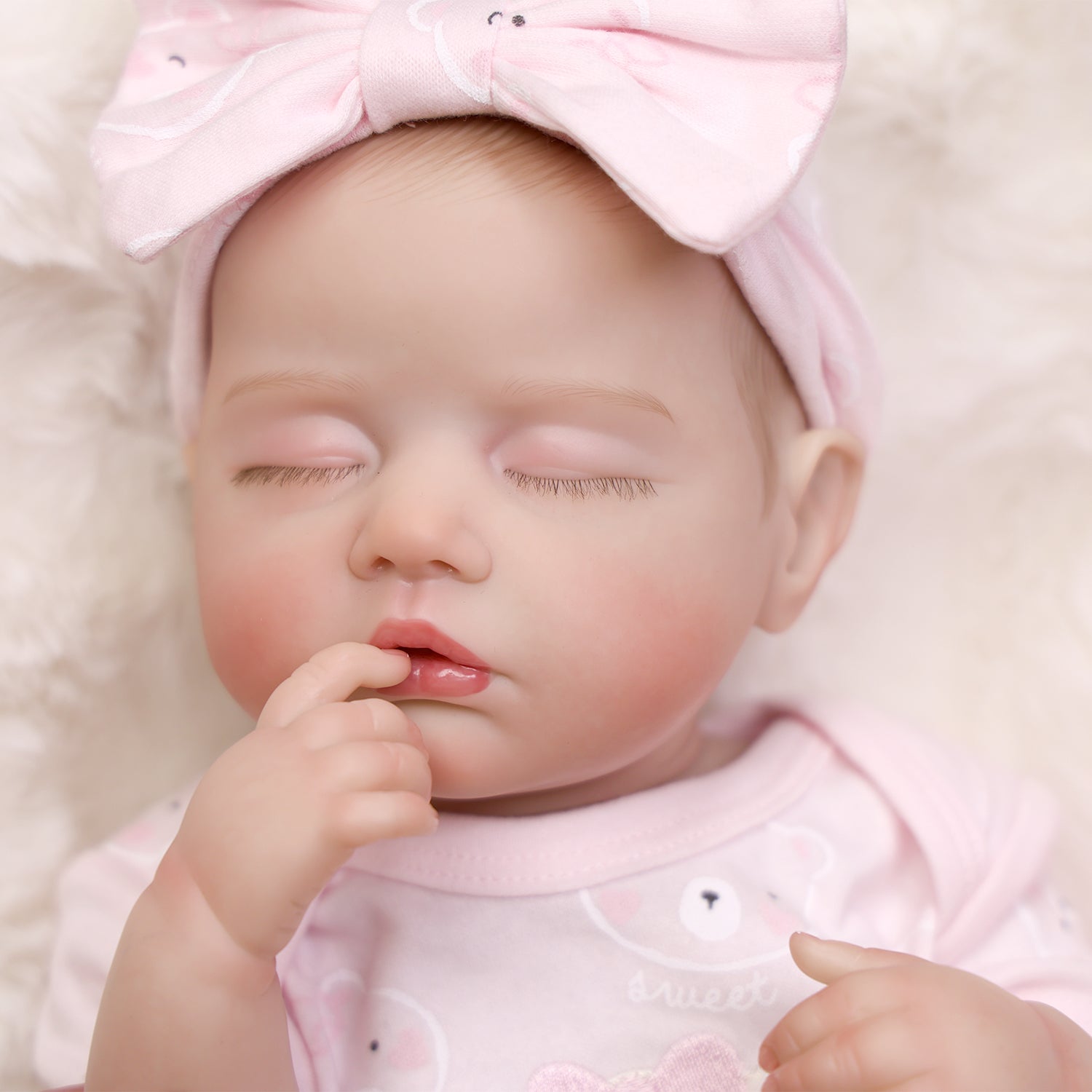 Realistic sleeping reborn doll in pink outfit, showing full body detail.