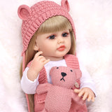 Blossom reborn doll sitting, showing full pink knitted overalls and hat.