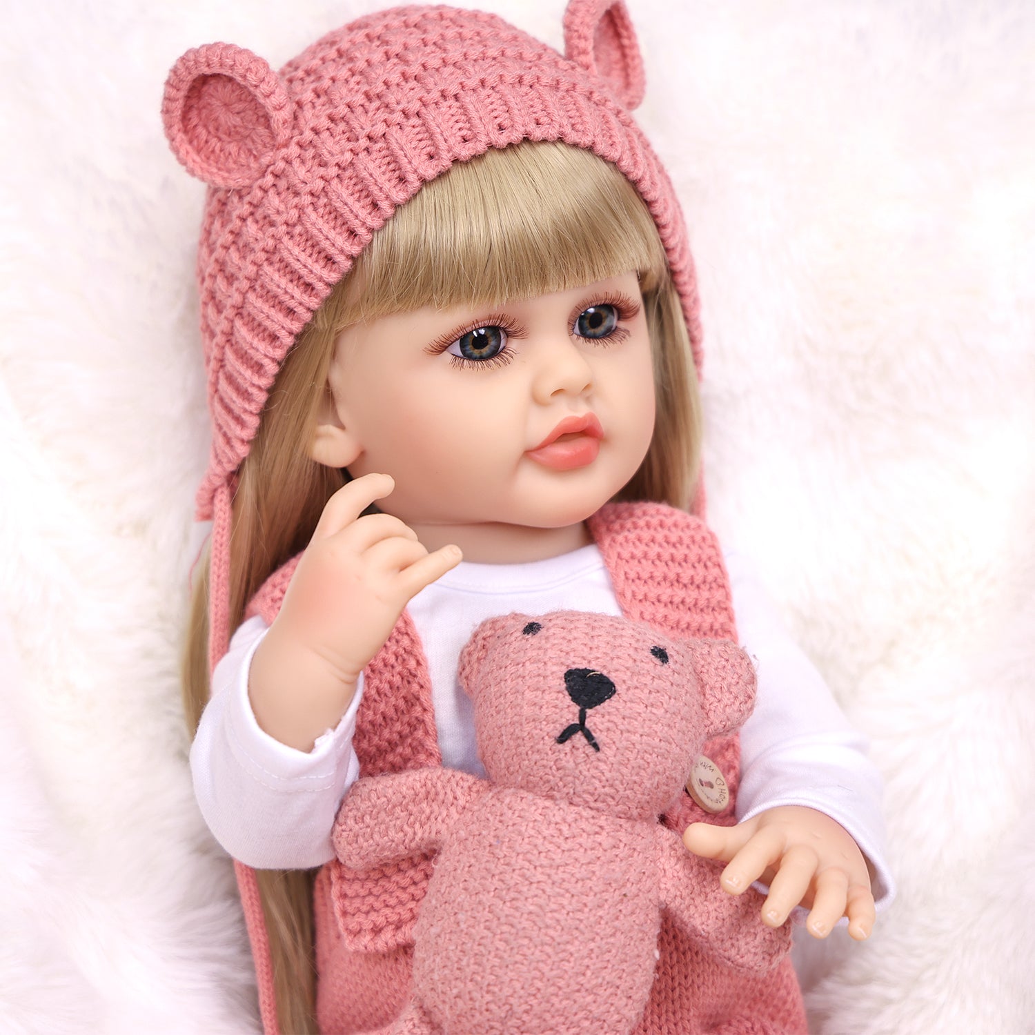 Blossom reborn doll sitting, showing full pink knitted overalls and hat.