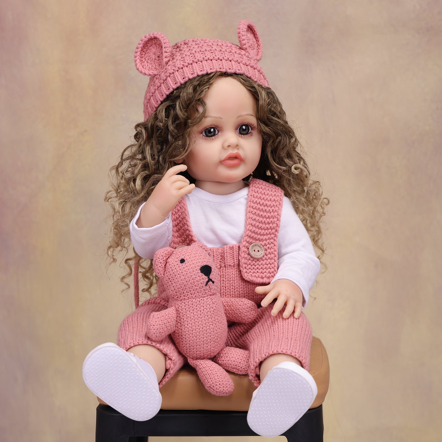 Realistic reborn baby doll wearing a pink knitted hat with bear ears.