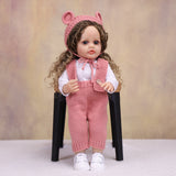 KEIUMI Sweetpea doll with pacifier, wearing pink knitted overalls.