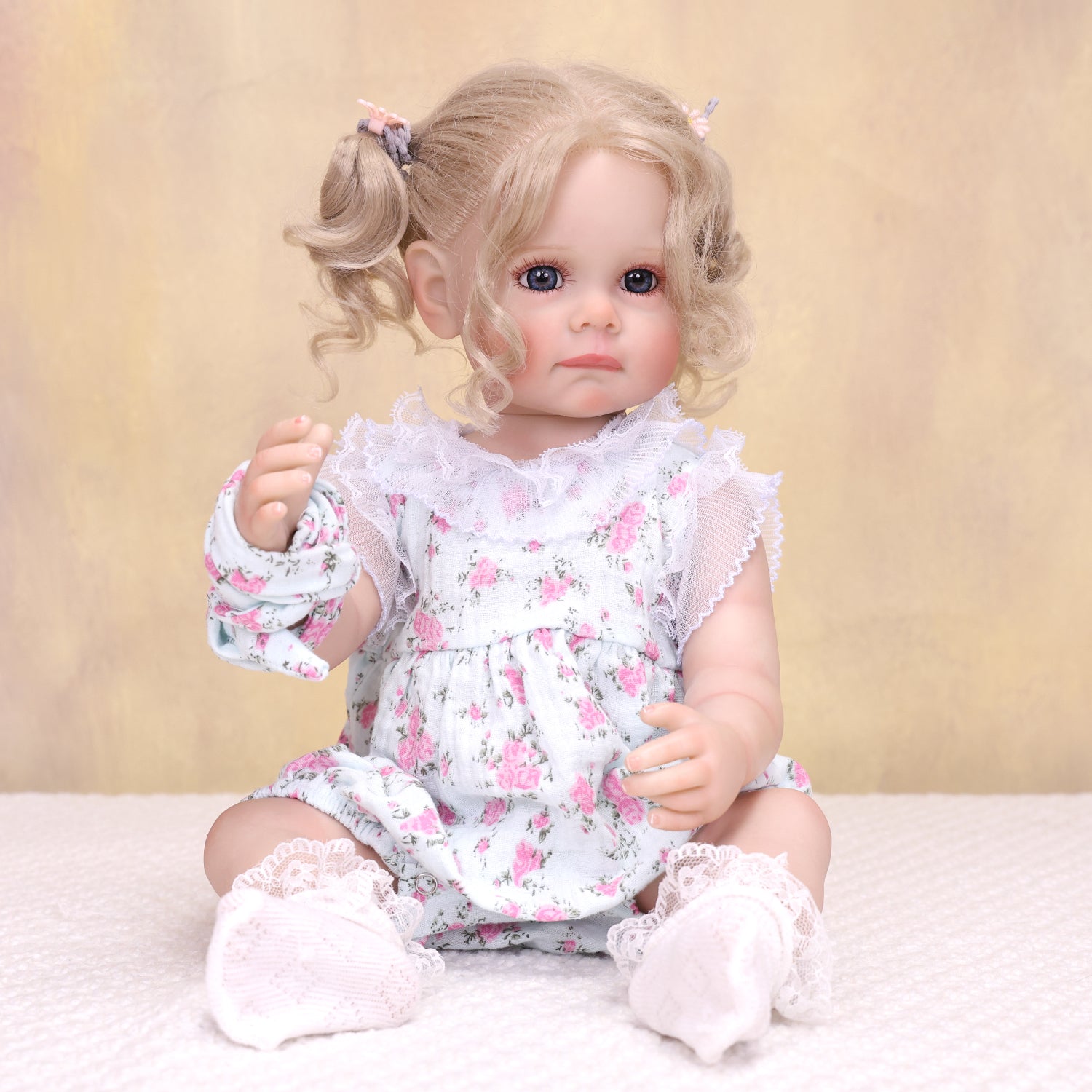 Pippa reborn doll sitting, wearing floral romper, with pacifier and bottle.