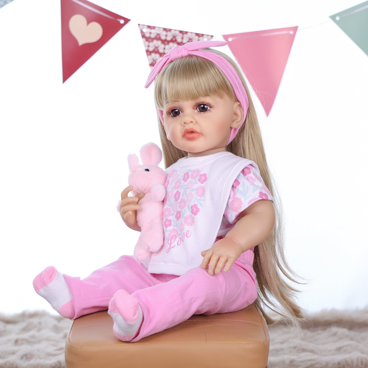 Joy reborn doll sitting, showing full pink floral outfit and accessories.