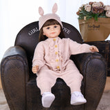 Poppy silicone reborn toddler doll in pink bunny hat outfit, sitting.