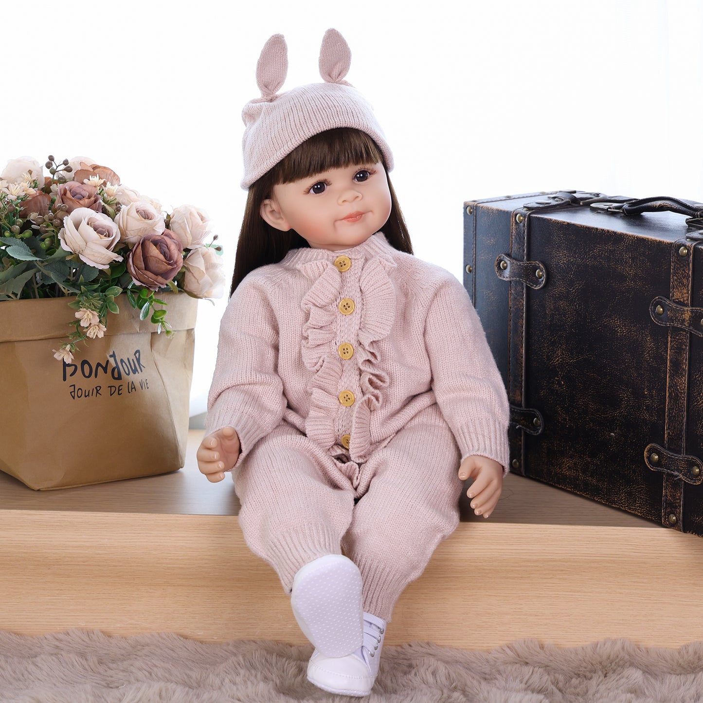Poppy reborn doll sitting, showcasing her full pink knitted romper and sneakers.