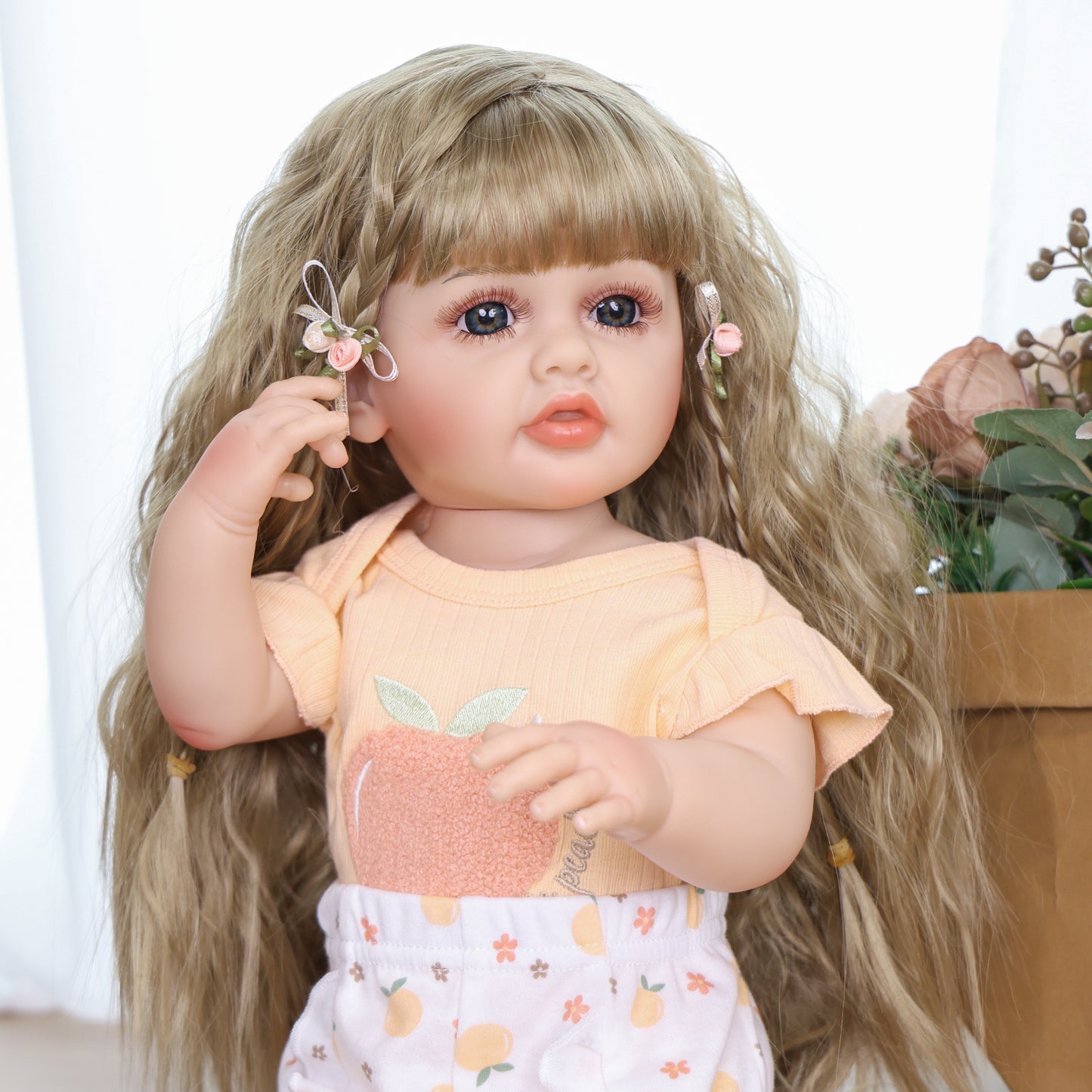 Peaches reborn doll sitting, showcasing her long blonde hair and floral clips.