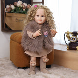 Sunny reborn toddler doll sitting, showcasing her ribbed beige dress and vest.