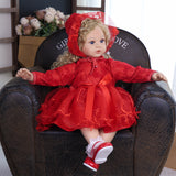 Ruby Belle toddler doll in full red ensemble, sitting with a white teddy bear.