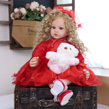Ruby Belle reborn doll looking charmingly at the camera, holding a teddy bear.